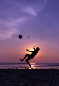Silhouette man playing with ball in background at sunset
