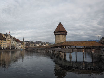 Covered bridge over river in city against cloudy sky