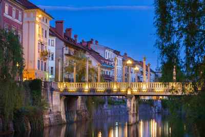 Illuminated bridge over river in city against sky at night