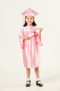 Portrait of cheerful girl wearing graduation gown against beige background