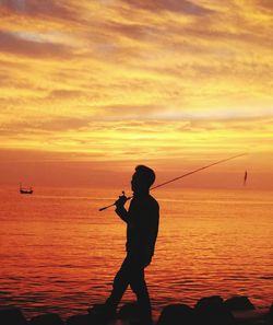 Side view of silhouette man standing on sea against sky during sunset