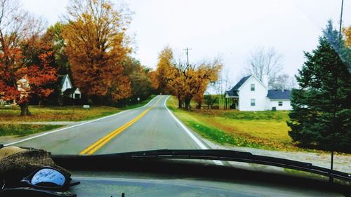 Road amidst trees against sky seen through car windshield