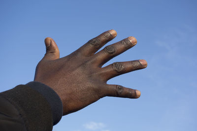 Low angle view of hand against blue sky