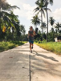 Young sportsman jogging on street amidst field against sky