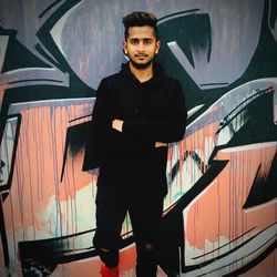 Portrait of young man standing against graffiti wall