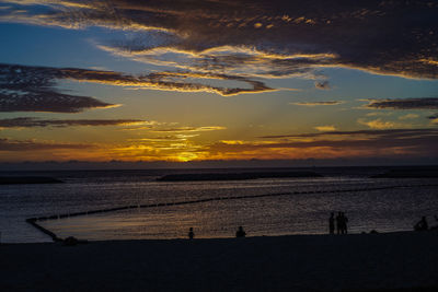 Silhouette people on beach against sky during sunset