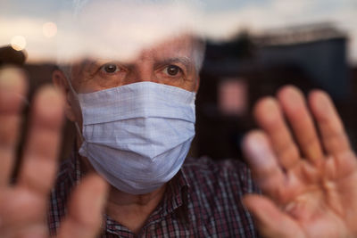 Senior man wearing mask standing by window at home