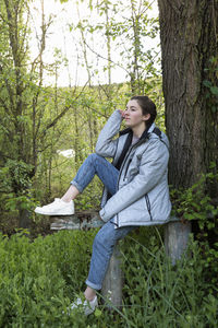 Woman sitting against trees in forest