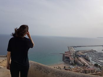 Rear view of woman standing on hill against harbor by sea