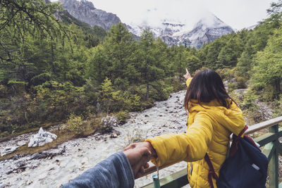 Woman gesturing while holding cropped man hand by river in forest