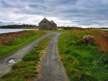 Dirt road amidst buildings against sky