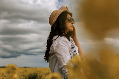 Side view of young woman standing against sky