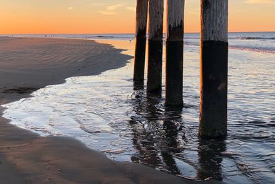 Wooden posts on beach against sky during sunset