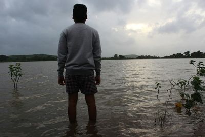 Rear view of man standing at beach against sky
