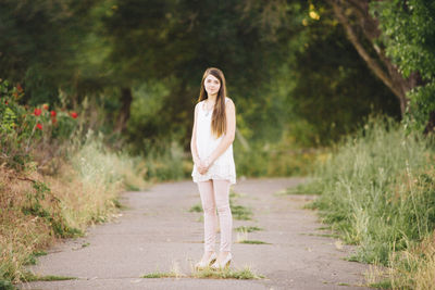 Portrait of young woman standing on footpath amidst grassy field