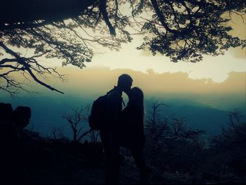 Silhouette couple romancing by trees on field at dusk