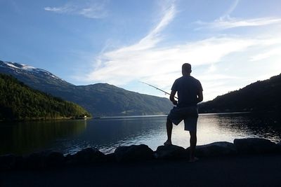 Rear view of man standing on lake against sky