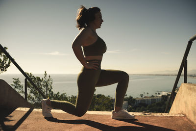 Girl doing lunges with the beach in the background person