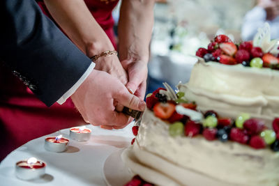 Cropped hands of newlywed couple cutting cake in wedding ceremony