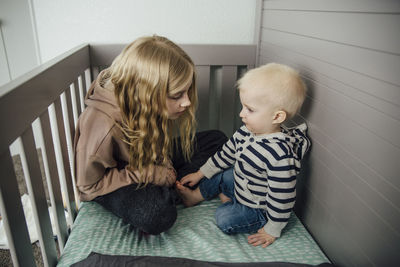 Girl with brother sitting in crib at home