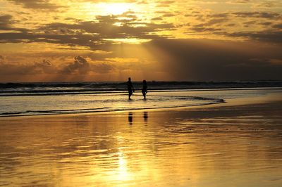 Silhouette people standing on beach against sky during sunset