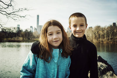 Portrait of smiling brother with arm around sister at lake in park