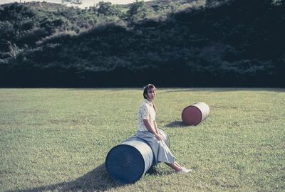Full length portrait of woman sitting on container in park