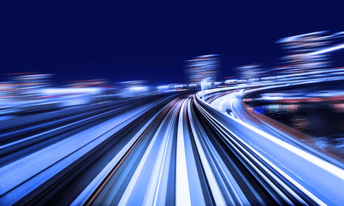 Light trails on illuminated city against sky at night