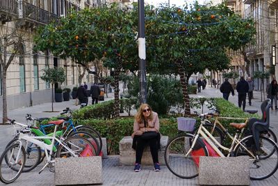 Full length of woman wearing warm clothing sitting by bicycles in city