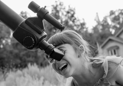 Happy girl looking through telescope outdoors