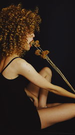 Close-up of woman with plants sitting against black background