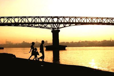 Silhouette of bridge over river during sunset