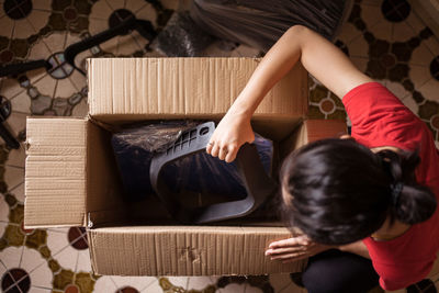 Top view of anonymous female taking parts of chair from carton box before assembling furniture at home