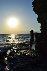 Woman standing on rock by sea against sky during sunset