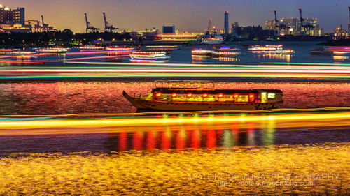 Blurred motion of illuminated bridge over river in city at night