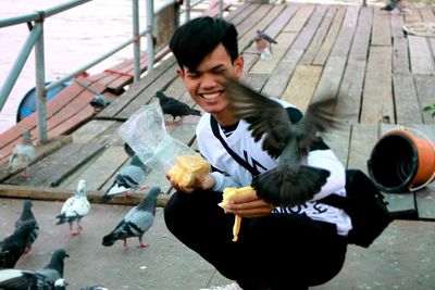 Young man feeding pigeons on pier