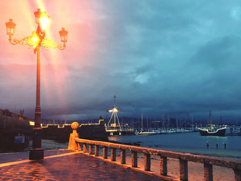 Illuminated pier over sea against cloudy sky