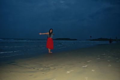 Woman with arms outstretched standing at beach against sky
 