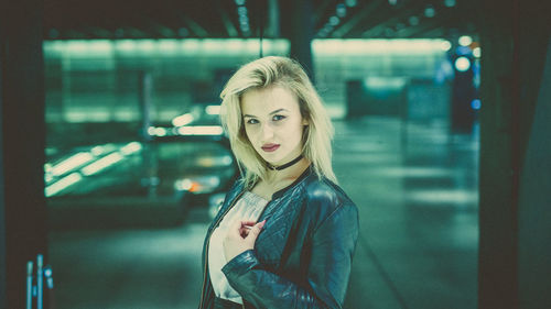 Portrait of young woman standing against illuminated wall