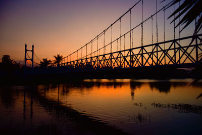 Silhouette bridge over river against sky during sunset