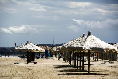 Thatched roofs on sand at beach against sky