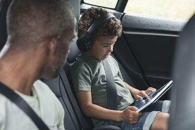 Man looking at son watching video on digital tablet in electric car