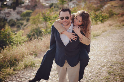 Portrait of man giving piggy back ride to happy woman standing on land