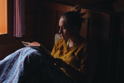 Woman reading book on bed in wooden cottage