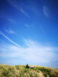 Mature man sitting on landscape against blue sky