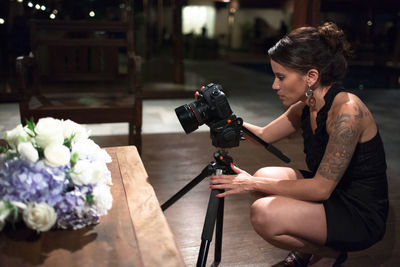 Young woman photographing with camera while sitting on wall