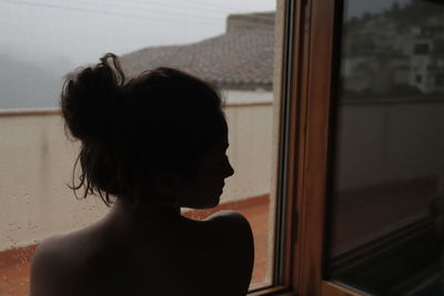 Rear view of girl against window at home