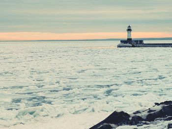 Lighthouse by sea against sky during sunset