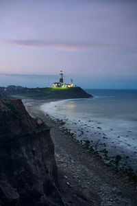 Lighthouse by sea against sky during sunset