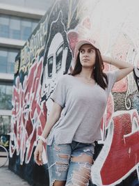 Portrait of young woman standing against graffiti wall